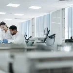 Laboratuvarda koruyucu ekipmanlarla çalışan iki bilim insanı eş araştırma sürecinde